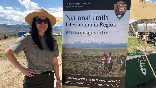 A uniformed park ranger stands next to a tall banner.