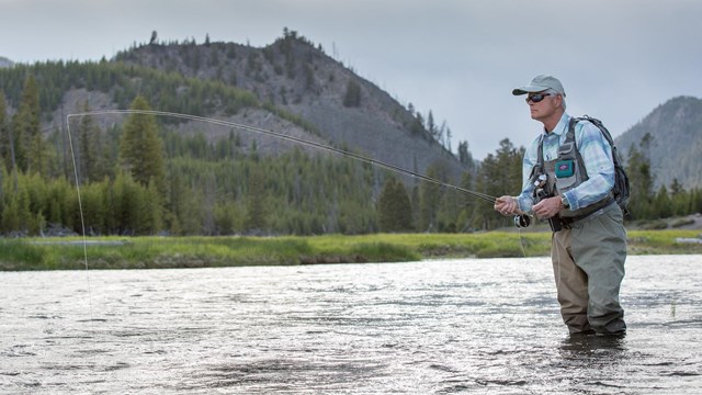Angler fishing in a river with a mountain in the background.
