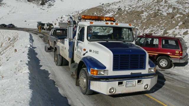 A wrecker hauls a broken down vehicle along a park road.