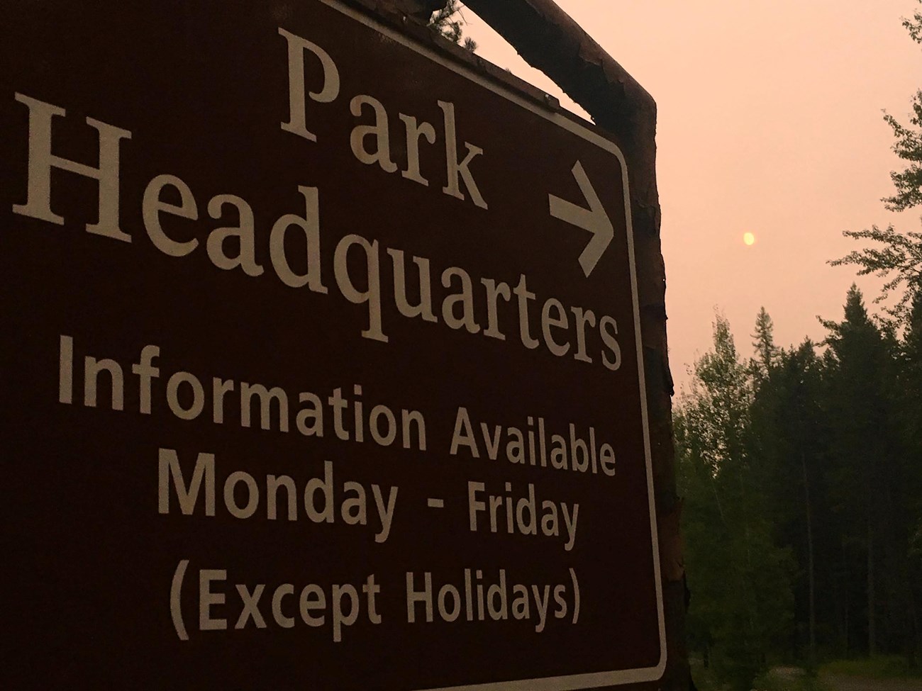 A photograph of Glacier National Park Headquarters sign with an arrow pointing.