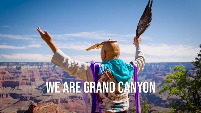 a man wearing ceremonial clothes is raising both arms while facing the colorful peaks and cliffs within Grand Canyon.